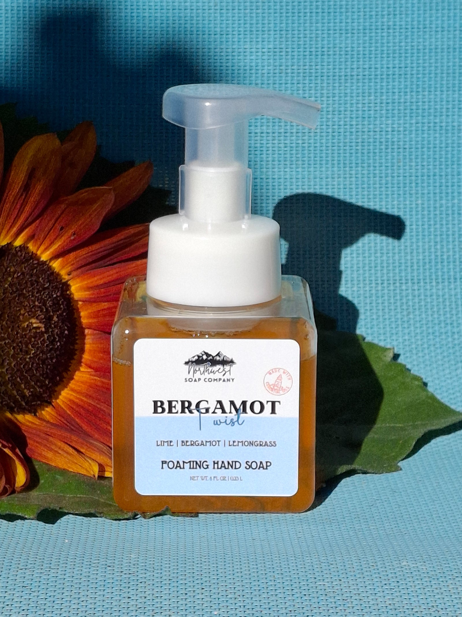 Hand soap bottle with a sunflower and green leaf on a textured blue background