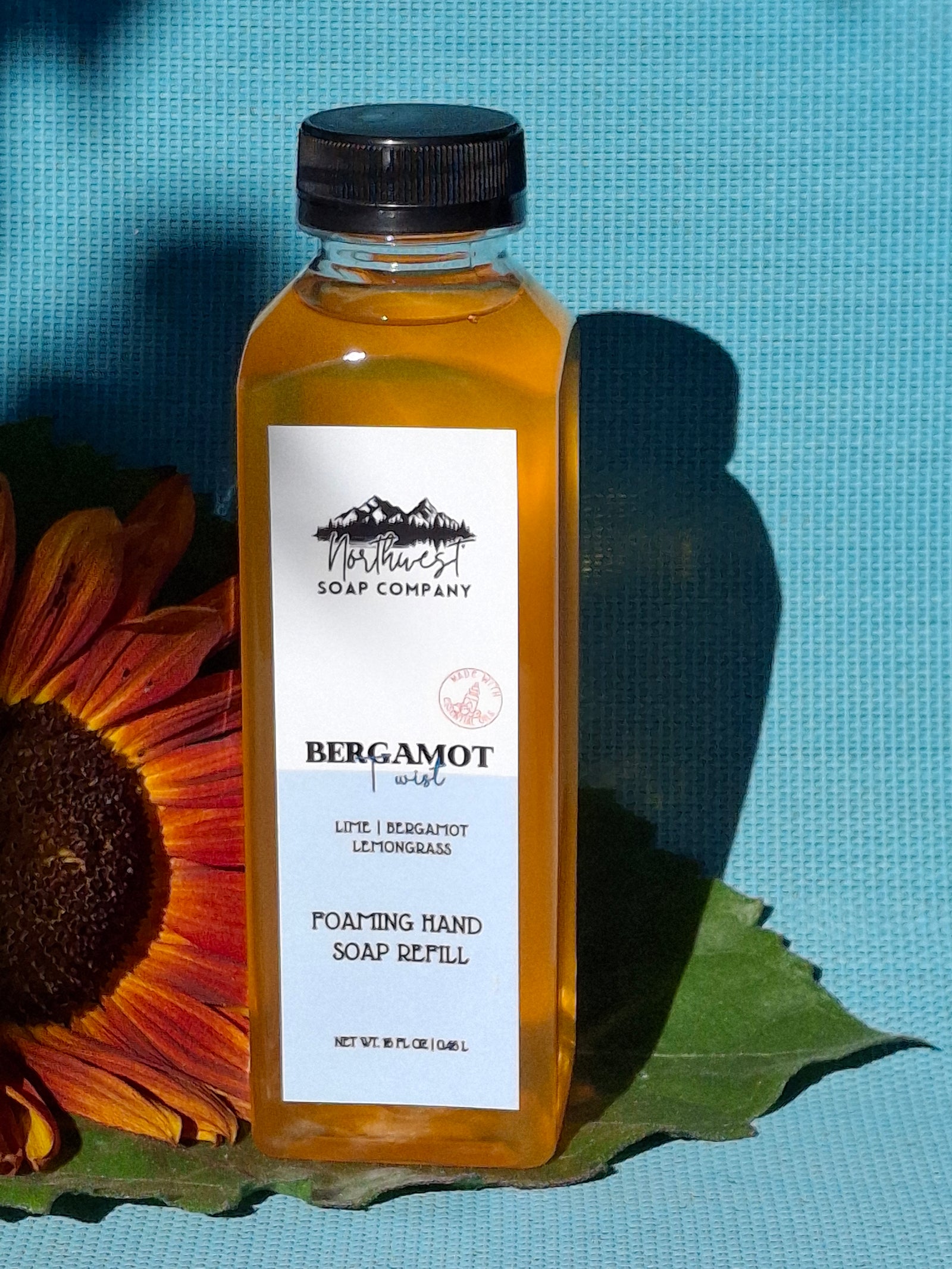 Bottle of bergamot soap with a sunflower and leaf on a blue background