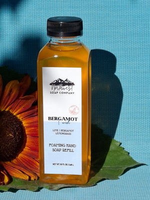 Bottle of bergamot soap with a sunflower and leaf on a blue background