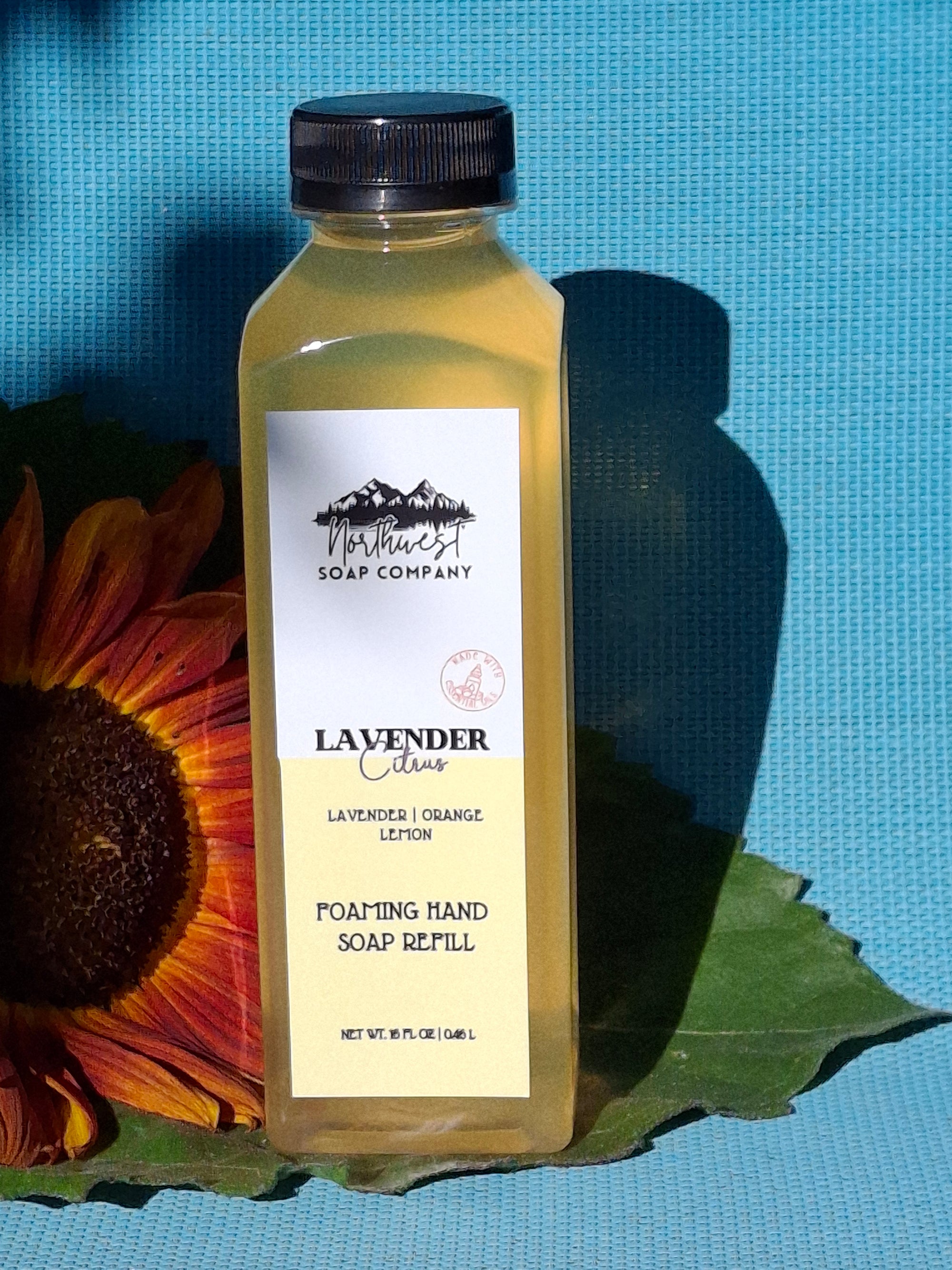 Bottle of lavender and citrus hand soap with a sunflower and green leaf on a blue background
