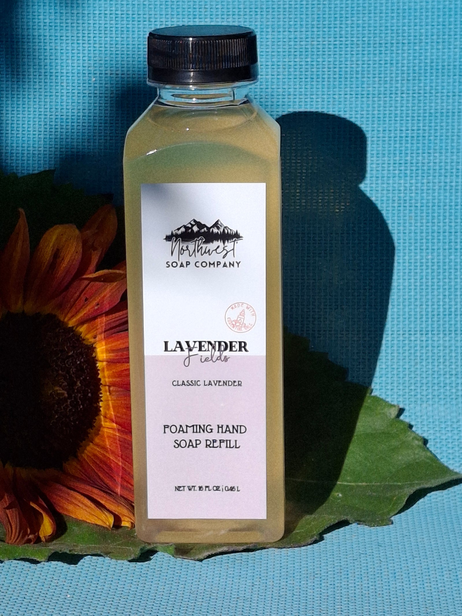 Bottle of bergamot soap with a sunflower and leaf on a blue background