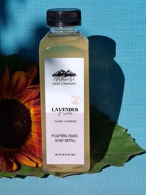 Hand soap bottle with lavender scent on a blue background with a sunflower and green leaves.