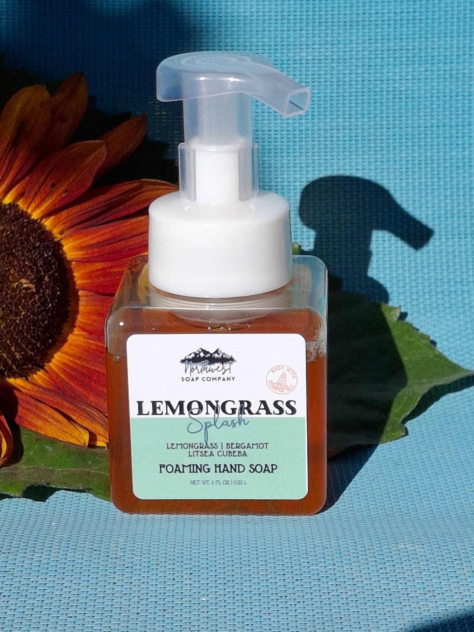 Foaming hand soap bottle with pump on a blue background with a sunflower and green leaves.