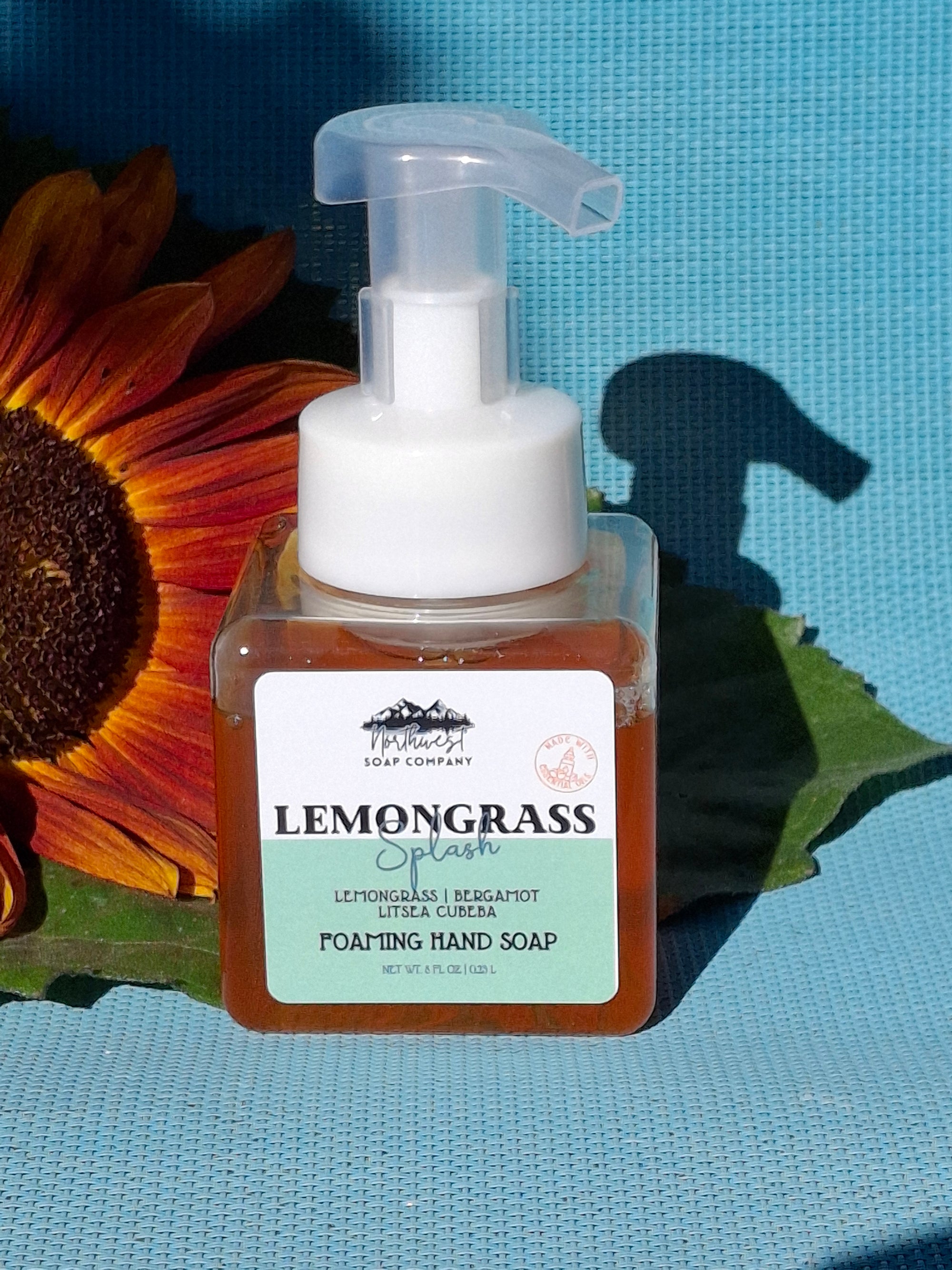 Foaming hand soap bottle with pump on a blue background with a sunflower and green leaves.