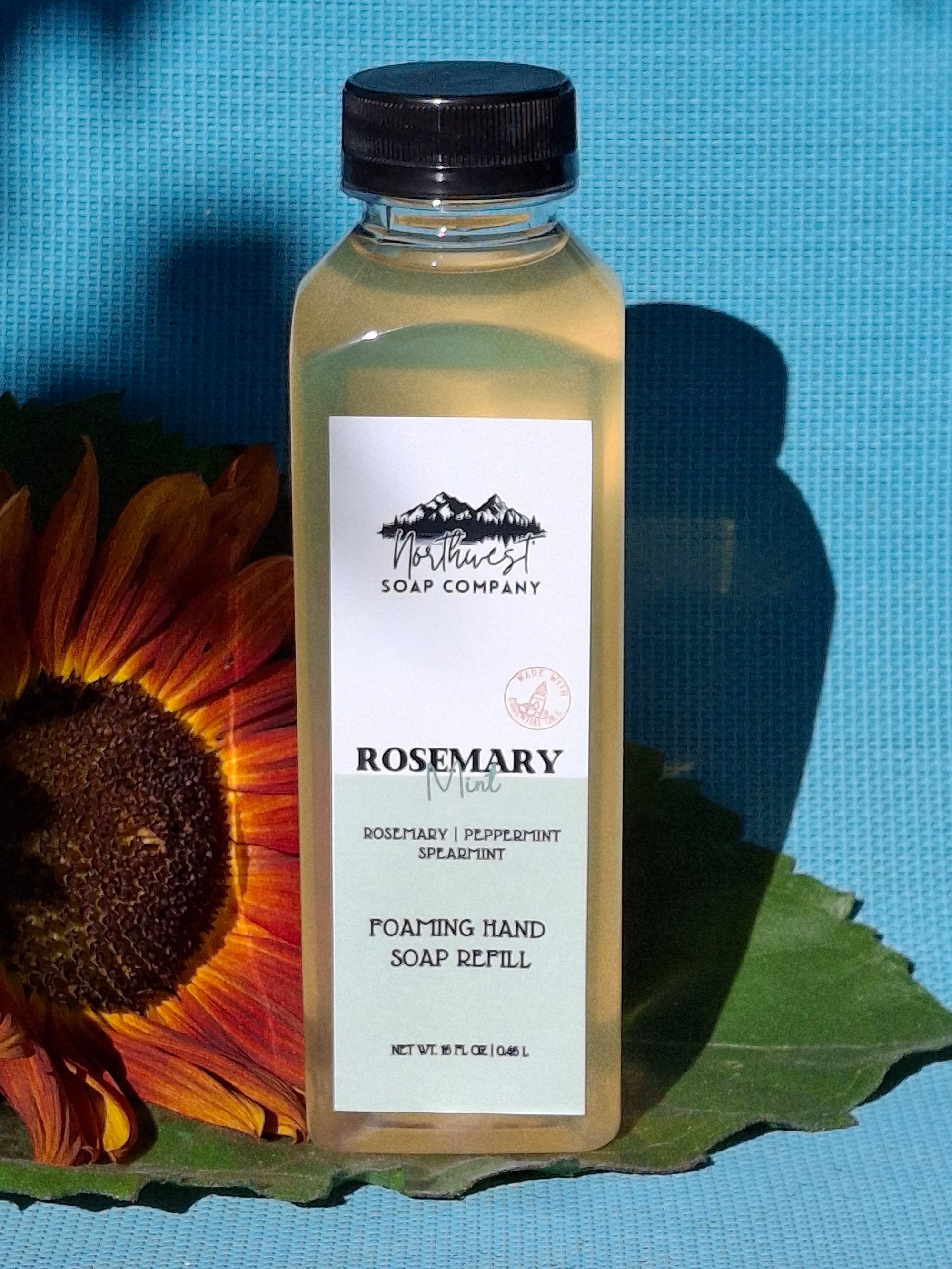 Bottle of Rosemary mint hand soap refill bottle with a sunflower and leaf on a blue background