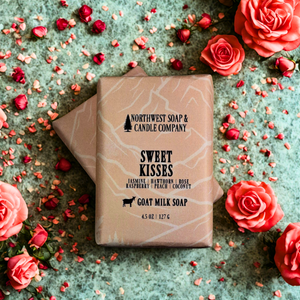 Goat milk soap bar from Northwest Soap & Candle Company surrounded by pink roses on a textured surface.