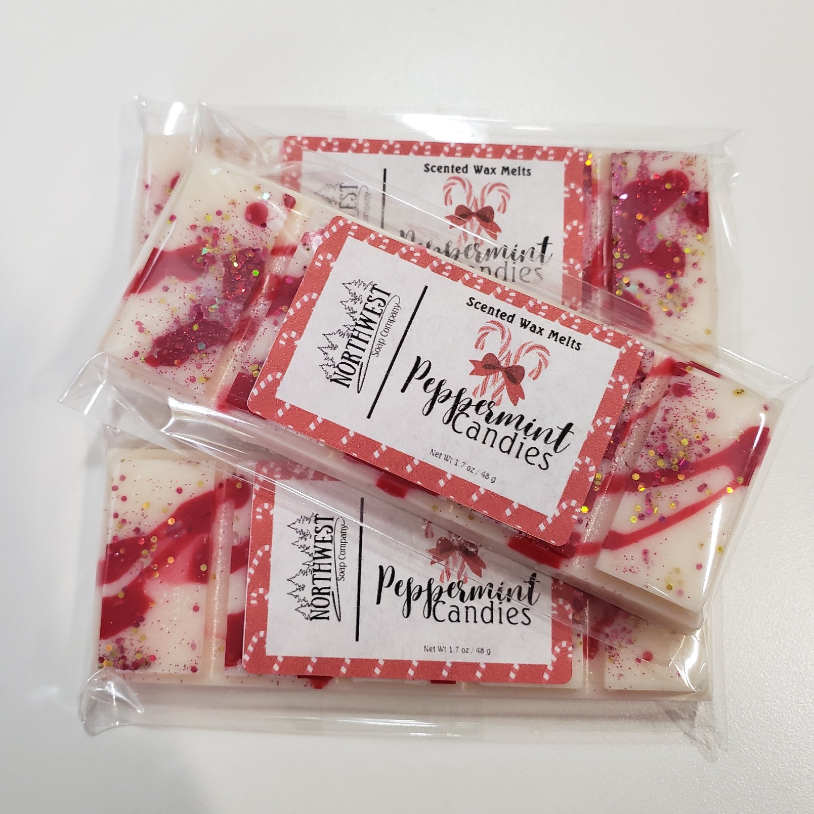 3 Peppermint Candies wax melts packaged in their recylable 5 PP wrappers.  Shaped like a candy bar in a white wax with red drizzle and eco glitter.